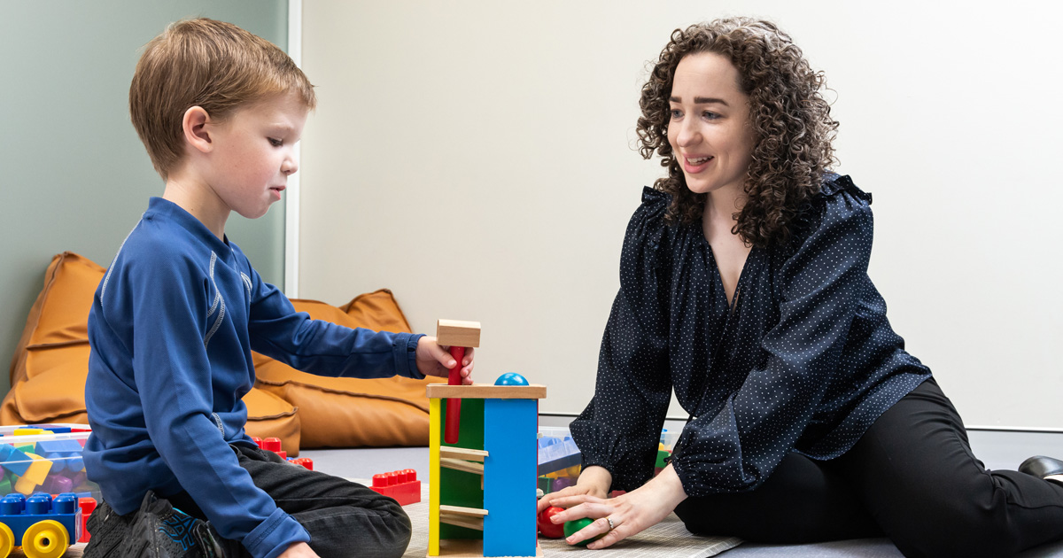A woman talking with a child who is playing with blocks